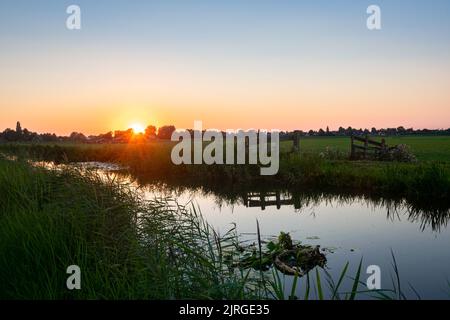 Die Sonne geht über der wässrigen holländischen Landschaft im westlichen Teil des Landes unter. Stockfoto