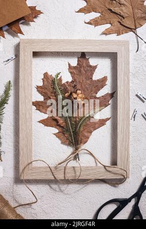 Bouquet aus getrocknetem gepresstem Blatt im Rahmen mit Schere, Seil und Notizbuch auf weißem Hintergrund. Hobby, handgemachte, florale Kunst und Boho-Stil Konzept. Stockfoto