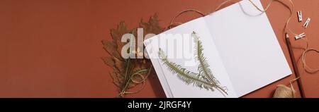 Getrocknetes gepresstes Blatt auf Papier aus Notizbuch mit Bleistift, Schere und Garn auf braunem Hintergrund. Hobby, Handarbeit, Blumenkunst und Boho-Konzept. Banner Stockfoto
