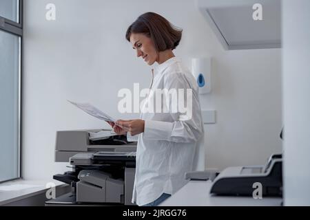 Lächelnde Arbeiterin scannt ein Dokument auf einem Kopiergerät in einem modernen Büro Stockfoto