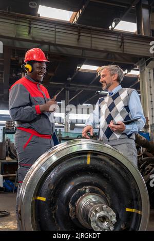 Lächelnde, multirassische Industriemitarbeiter stehen in Einer Eisenbahnfabrik neben den Rädern. Bereich Für Wartung, Reparatur Und Service Von Zügen Und Wag Stockfoto