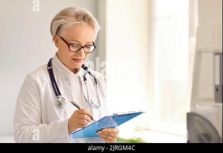 Ärztin mit einem Klemmbrett und Notizen in medizinischen Formularen und Dokumenten Stockfoto