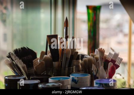 Selektiver Fokus auf künstlerische Werkstatt. Pinsel und Farbtöpfe auf dem Werkstatttisch malen. Stockfoto