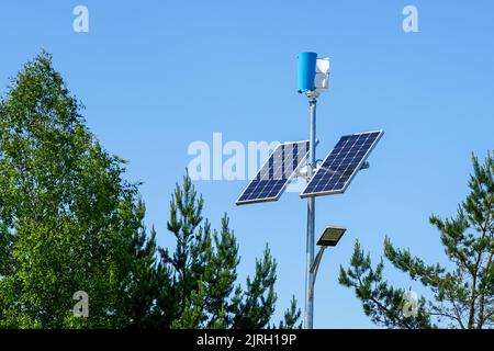 Stange mit innovativer LED-Straßenleuchte, die von Solarzellen und kleinem vertikalen Windgenerator mit blauem Himmel-Hintergrund angetrieben wird Stockfoto