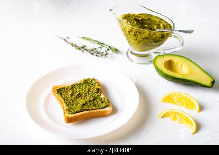 Toast mit Avocado und Chimichurri-Sauce auf einem weißen Teller. Gesundes vegetarisches Essen. Weißer Hintergrund. Stockfoto