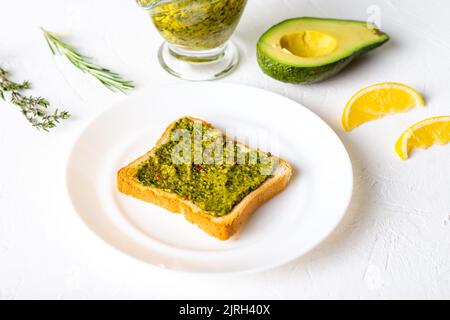 Toast mit Avocado und Chimichurri-Sauce auf einem weißen Teller. Gesundes vegetarisches Essen. Weißer Hintergrund. Stockfoto