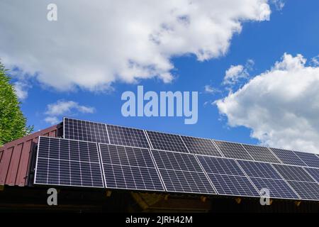 Viele Photovoltaik-Sonnenkollektoren auf Holzhausdach montiert, Hintergrund des blauen Himmels mit weißen Wolken, Dach von Solarzellen Stockfoto