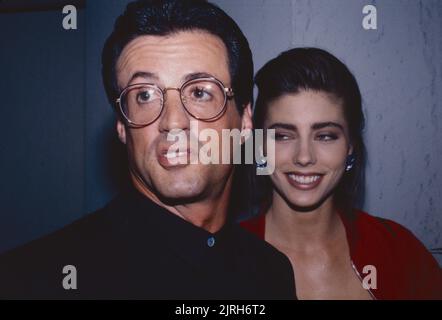 **DATEI FOTO** Jennifer Flavin Akten zur Scheidung von Sylvester Stallone. Sylvester Stallone und ihre Freundin Jennifer Flavin nehmen an einem Cocktailempfang Teil, der von Tina Brown zur Eröffnung der Versace Boutique in New York City am 24. April 1990 veranstaltet wird. Foto: Henry McGee/MediaPunch Stockfoto