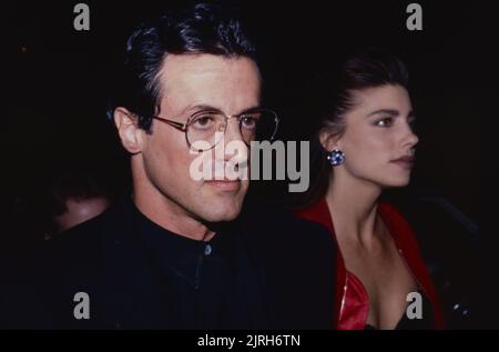 **DATEI FOTO** Jennifer Flavin Akten zur Scheidung von Sylvester Stallone. Sylvester Stallone und ihre Freundin Jennifer Flavin nehmen an einem Cocktailempfang Teil, der von Tina Brown zur Eröffnung der Versace Boutique in New York City am 24. April 1990 veranstaltet wird. Foto: Henry McGee/MediaPunch Stockfoto