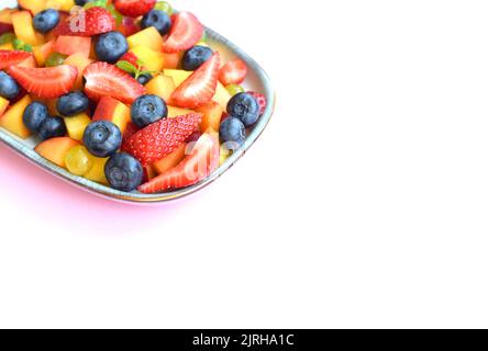 Obstsalat auf einem rechteckigen Teller auf weißem Hintergrund. Erdbeeren, Pfirsiche und Heidelbeeren in Scheiben geschnitten mit Minzblättern. Stockfoto