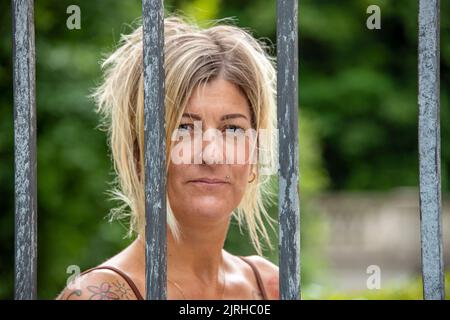 Kopfaufnahme einer blonden europäischen Frau mit Gesichtsausdruck hinter Gittern Stockfoto