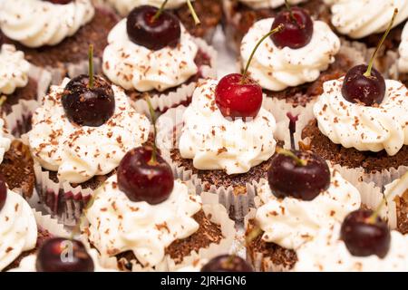 Hausgemachte Cupcakes aus Schokolade mit Schlagsahne, frischen Kirschen und geriebener Schokolade. Stockfoto