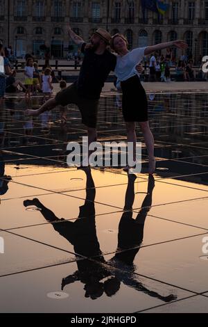 Bordeaux, Frankreich - Juli, 17: Ein paar Verliebte bei Sonnenuntergang haben Spaß beim Spazieren im Wasserspiegelbrunnen am Place de la Bourse in Bordeaux, Aquitanien Stockfoto