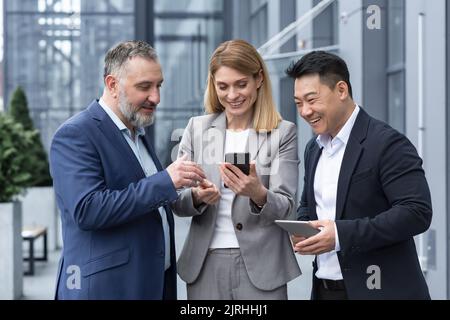 Drei Kollegen Mitarbeiter sehen lustige Videos oder sehen sich Fotos, Bilder Erinnerungen Blick auf Smartphone-Bildschirm mit dem Handy. Gruppe von Geschäftsleuten Büroangestellte Spaß in den Pausen Stockfoto