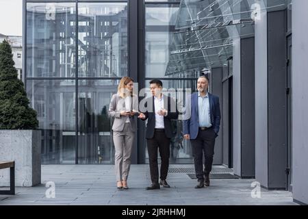 Drei verschiedene Geschäftsleute, die konzentriert und nachdenklich außerhalb des Bürogebäudes gehen und sprechen, Männer und Frauen, diskutieren Pläne und Arbeitsprojekt Stockfoto
