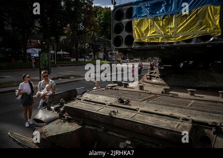 Kiew, Ukraine. 22. August 2022. Eine Familie beobachtet in Kiew das Wrack eines russischen Multi-Rocket Launch Systems (MLRS) mit ukrainischer Nationalflagge. Zum bevorstehenden Unabhängigkeitstag der Ukraine und fast 6 Monate nach der umfassenden Invasion der Ukraine am 24. Februar veranstaltet die Hauptstadt Kiew in der Hauptstraße der Chreschajtk-Straße eine Ausstellung mit mehreren zerstörten Militärgeräten, Panzer und Waffen der Streitkräfte der Russischen Föderation (AFRF).als die russische vollständige Invasion der Ukraine am 24. Februar begann, hat der Krieg, der zahlreiche c getötet hat Stockfoto