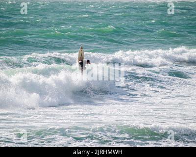 Raglan, Neuseeland -Juni 7 2008 ein eingefräunter Surfer, der am wilden Tag senkrecht aus den Wellen zeigt. Stockfoto