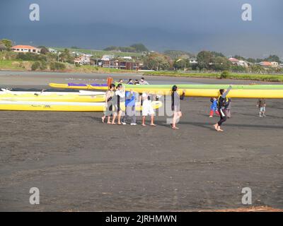 Raglan, Neuseeland -Juni 7 2008 die Gruppe arbeitet zusammen und trägt Waka-ama oder Kanus auf ihren Schultern am Ufer von Raglan Stockfoto