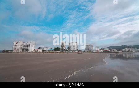 Bahia de Caraquez, Manabi / Ecuador - August 19 2022: Menschen gehen und spielen am Strand vor der Promenade mit modernen Eigentumswohnungen in Th Stockfoto