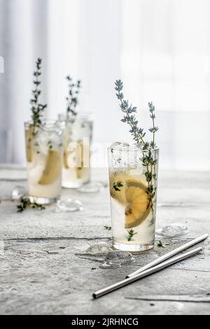 Cocktail mit Zitrone, Thymian und Eis in Gläsern auf dem Tisch. Erfrischungscocktail oder infundiert mit Wasser Stockfoto