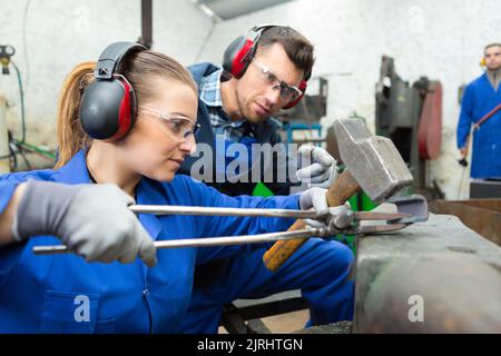 Frau, die Metall in Zangen über Amboss gehämmern Stockfoto