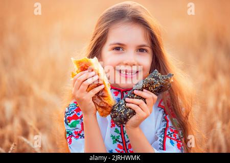 Bulgarisches Mädchen, schöne Frau, essen frisch gebackene Banitsa, Käsekuchen während der Ernte in goldenen Weizenfeld Stockfoto