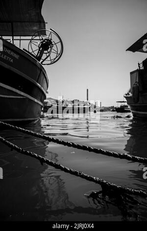 Eine vertikale Aufnahme von Wasser und Fragmenten von Schiffen auf einem Hafen in Graustufen Stockfoto