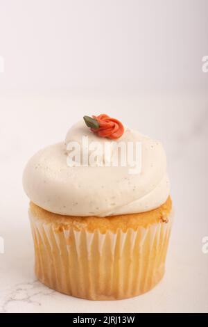 Eine Nahaufnahme eines Vanille-Cupcake mit Buttercreme-Zuckerguss und Blume Stockfoto