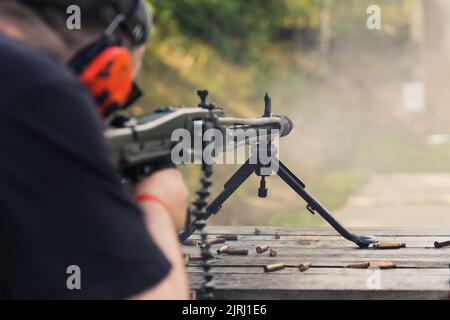 08.07.2022 Warschau, Polen unkenntliche kaukasische Person in roten Schutzohrhörern, die mit einem Maschinengewehr schießen. Wettbewerb auf Schießstand. Schusswaffenkonzept. Hochwertige Fotos Stockfoto