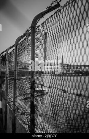 Eine selektive Fokusaufnahme eines Gitterzauns an einem Hafen in Graustufen Stockfoto