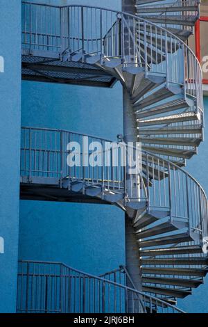 Spiralförmige Stahltreppe an der Außenseite eines mit blauem Stuck bekleideten modernen Architekturgebäudes in Prag, Tschechische Republik. Stockfoto