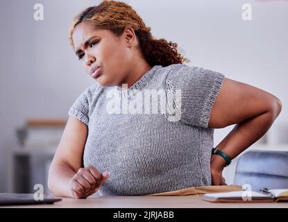 Mitarbeiter im Unternehmen, die an Rückenschmerzen leiden, während sie an einem Schreibtisch im Büro arbeiten, unbequem und besorgt. Junge Berufserfahrung Stockfoto