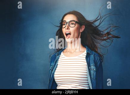 Der Surround Sound-Effekt. Studioaufnahme einer jungen Frau mit Luft, die vor blauem Hintergrund in ihr Gesicht geblasen wird. Stockfoto