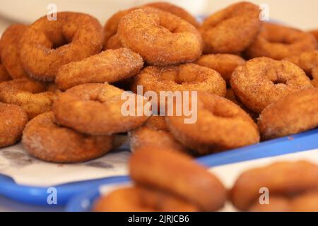 Eine Reihe von frischen, goldgebratenen Zimtzucker-Donuts oder Donuts, die auf einem blauen Blech und Backpapier gestapelt sind Stockfoto