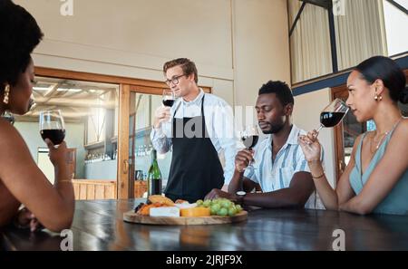 Gastfreundschaft, Luxus und Weinverkostung in einem Restaurant mit einem professionellen Sommelier, der lehrt, wie man Rotwein genießt. Eine vielfältige Gruppe, die Spaß hat Stockfoto