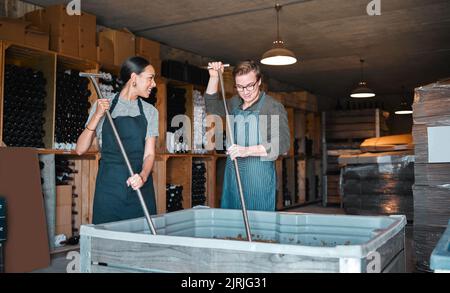 Mitarbeiter der Weinkellerei, die Wein mit einem Werkzeug oder einer Ausrüstung für die Obstpresse im Lager oder in der Destillerie anstellen. Frau und Mann Winzer oder Fabrikanten drücken Saft Stockfoto