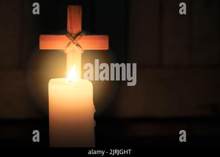 Die Kerze leuchtet vor dem Kreuz. Weihnachten, Ostern und religiöser Hintergrund mit Kopierraum. Stockfoto