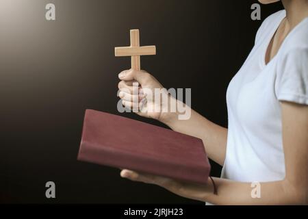 Hände mit Holzkreuz über der offenen heiligen russischen bibel auf dem Hintergrund des Sonnenaufgangs, Kruzifix, Symbol des Glaubens. Stockfoto