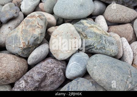 Große Steine in verschiedenen Formen am Flussufer aus der Nähe. In der Nähe gibt es viele kleine Steine. Stockfoto