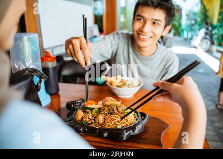 Mann, der Essstäbchen hält und gebratene Hühnernudeln nimmt Stockfoto