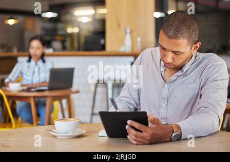 Freiberuflicher, geschäftlicher und Coffee Shop eines Mannes, der in einem Restaurant arbeitet und Remote-Arbeit für sein Startup leistet. Junger männlicher Unternehmer mit einem Tablet Stockfoto