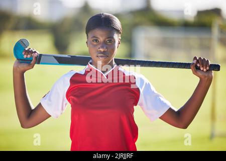 Hockeyspieler oder Trainer halten Stock bereit für einen Wettbewerb oder ein Spiel auf dem Sportplatz oder Feld. Porträt einer ernsthaften, fitteren und aktiven schwarzen Frau Stockfoto