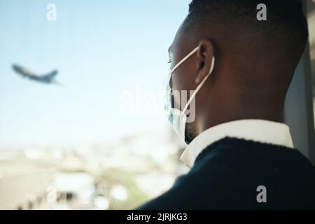 Geschäftsmann auf einem Flughafen für Arbeitsreisen während covid mit einer Maske und Flugzeug fliegen im Hintergrund. Unternehmer, Mitarbeiter oder Unternehmensmitarbeiter Stockfoto