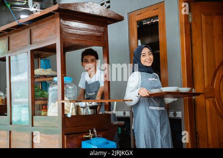 muslimische Verkäufer in Schürze Vorbereitung Hühnernudeln Gericht mit Schüsseln Stockfoto