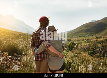 Erklimmen Sie einen Berg, um zum guten Leben zu gelangen. Rückansicht eines jungen Paares, das einen Bergblick in der Natur bewundert. Stockfoto