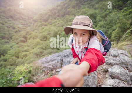 Helfende Hand. Wanderer Frau bekommen Hilfe auf Wanderung lächelnd glücklich Überwindung Hindernis. Tourist Backpacker zu Fuß auf dem Moutain, Junges Paar unterwegs. Stockfoto
