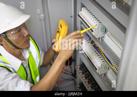 Ein Elektriker arbeitet in einer Schalttafel mit elektrischen Anschlüssen, die Geräte mit einem komplexen Arbeitskonzept verbinden. Stockfoto