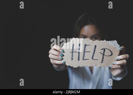 Frauen sitzen allein mit depressiver Expression und zeigen ein Papier mit einem Hilfetext. Schluss mit Gewalt gegen Frauen. Stockfoto