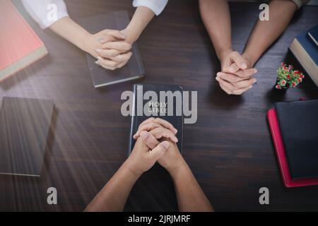 Eine Gruppe asiatischer Christen sitzt in einer katholischen Kirche und betet für den Segen Gottes, die blasse Sonne scheint am Ort der Anbetung mit Kopierraum. Stockfoto