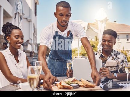 Der Kellner servierte Essen für Paare in einem Restaurant, der Arbeiter gab Service und im Sommer Essen auf dem Tisch in einem Café. Fröhlicher Mann und Frau, die in einem Geschäft zu Mittag essen Stockfoto